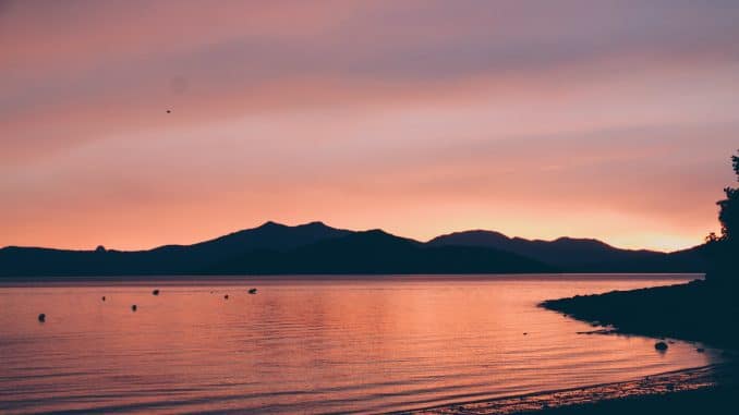 silhouette of mountain near body of water during sunset